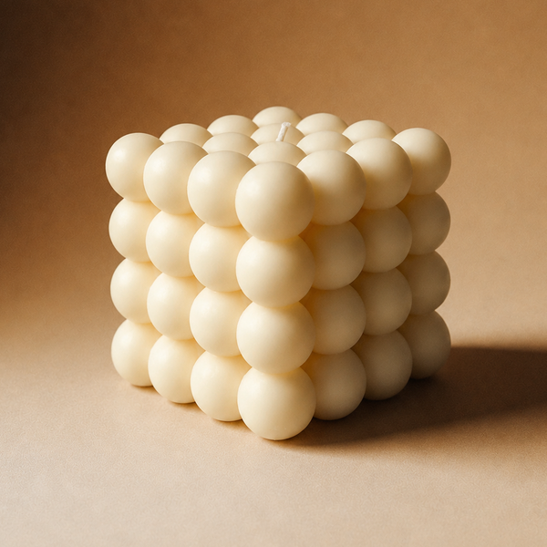 A cube-shaped bubble candle made of 3D spherical wax clusters, shown on a warm brown textured background.