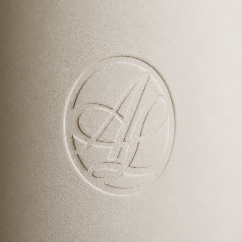 A close-up of a textured beige surface featuring an embossed circular monogram logo with stylized interlocking letters.