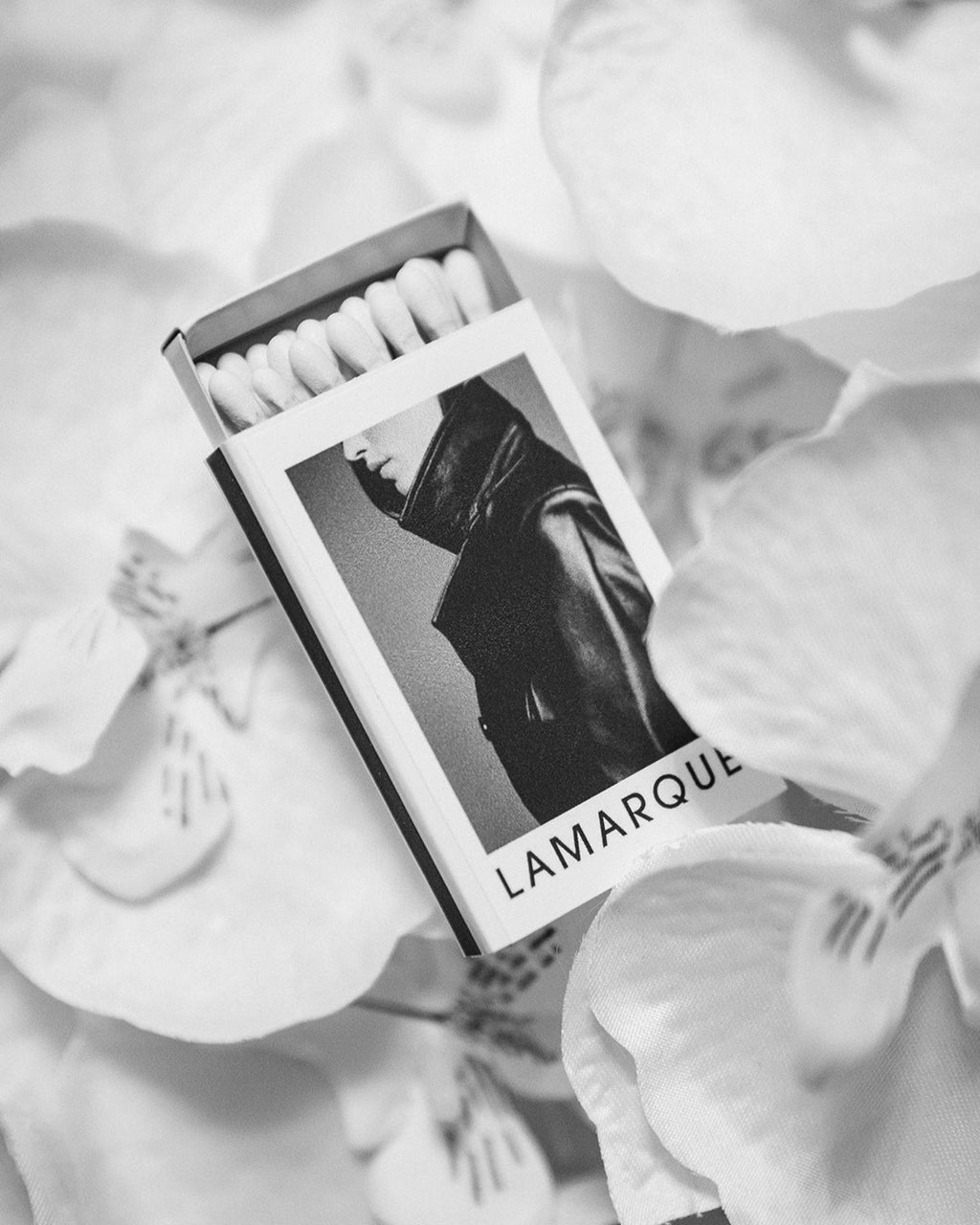 A matchbox with a custom design, featuring a black and white illustration, branded logo and image placed on a floral surface.