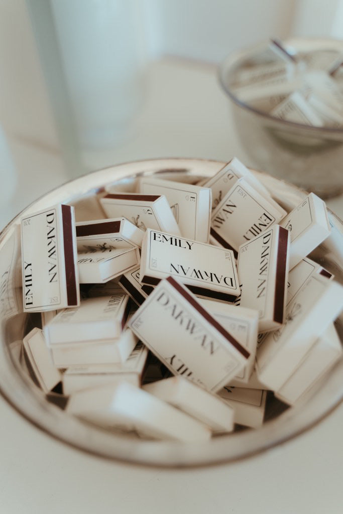 A collection of black and white personalized name matchboxes with double-sided designs, placed in a silver bowl.